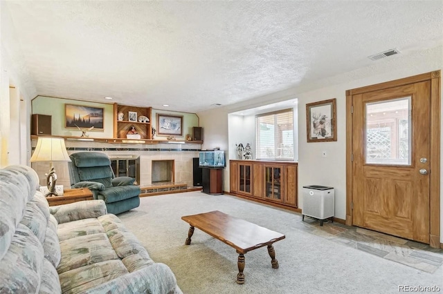 living room featuring light colored carpet, a textured ceiling, a fireplace with raised hearth, and visible vents