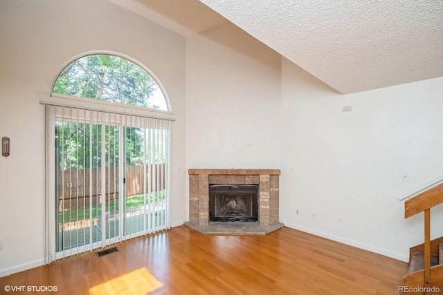 unfurnished living room with high vaulted ceiling, wood-type flooring, a textured ceiling, and a brick fireplace