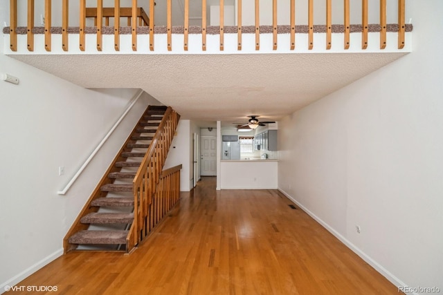 staircase featuring wood-type flooring, a textured ceiling, and ceiling fan