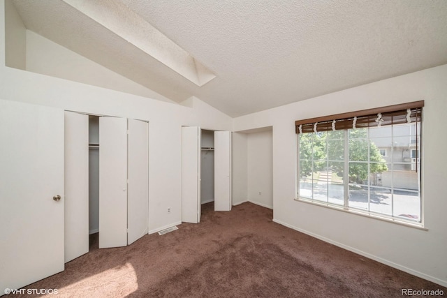 unfurnished bedroom featuring carpet flooring, lofted ceiling with skylight, a textured ceiling, and two closets