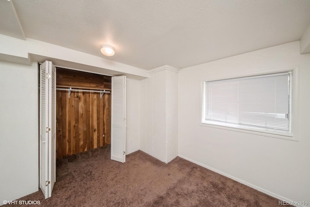 unfurnished bedroom with a textured ceiling, dark carpet, and a closet