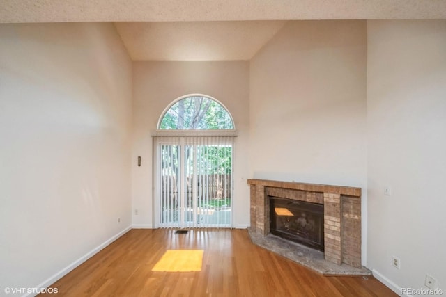 unfurnished living room featuring hardwood / wood-style flooring, vaulted ceiling, and a brick fireplace