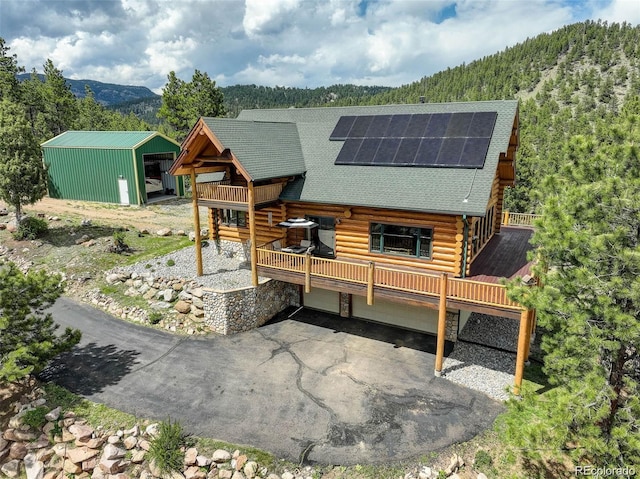 rear view of house featuring solar panels, an outdoor structure, a garage, and a deck