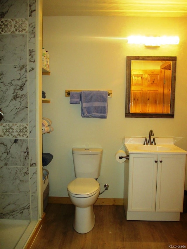 bathroom with vanity, toilet, a tile shower, and wood-type flooring