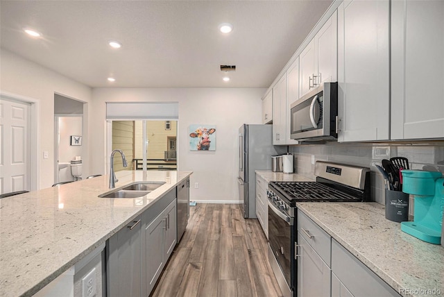 kitchen with light stone counters, wood finished floors, a sink, stainless steel appliances, and backsplash