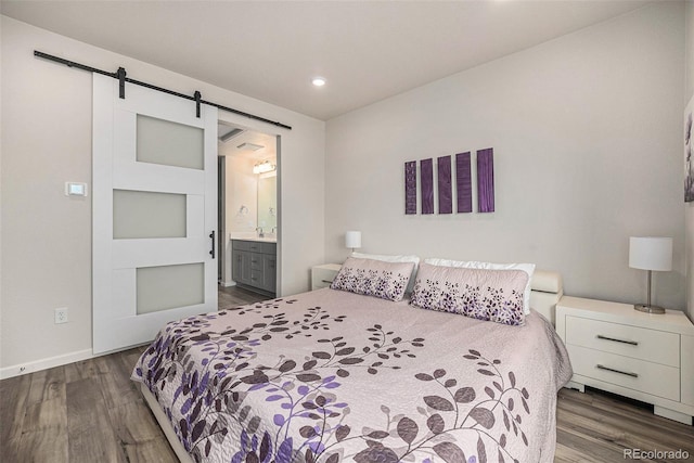 bedroom featuring ensuite bath, a barn door, wood finished floors, and baseboards