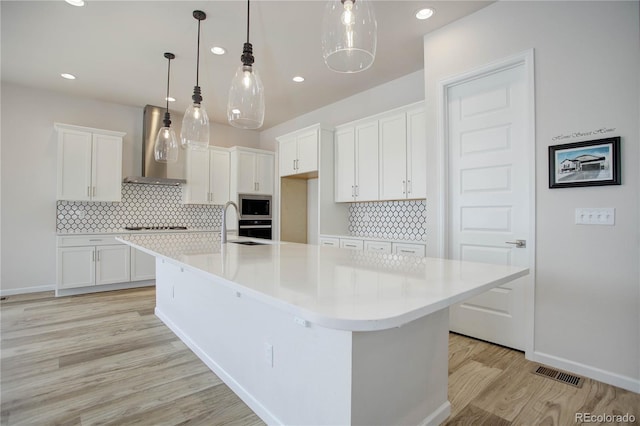 kitchen with wall chimney range hood, a spacious island, and white cabinetry