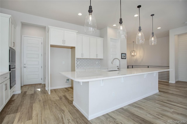 kitchen with light hardwood / wood-style floors, hanging light fixtures, sink, white cabinetry, and a large island