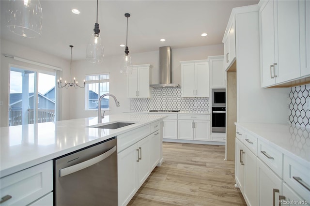 kitchen with light wood-type flooring, an inviting chandelier, sink, appliances with stainless steel finishes, and wall chimney range hood