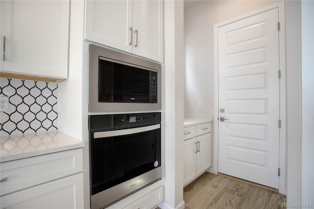 kitchen featuring built in microwave, stainless steel oven, white cabinetry, and light hardwood / wood-style floors