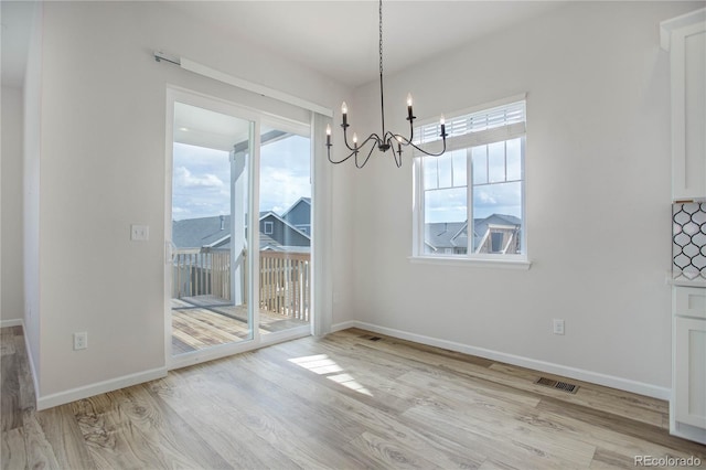 unfurnished dining area with plenty of natural light, a notable chandelier, and light wood-type flooring