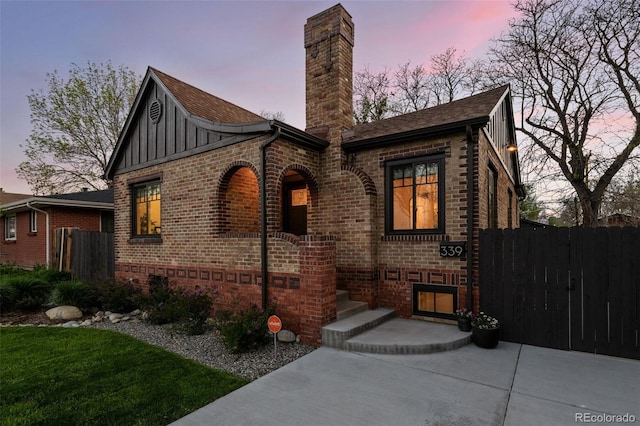 view of front of house featuring board and batten siding, brick siding, fence, and a chimney