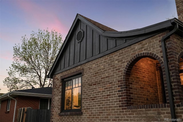 property exterior at dusk featuring board and batten siding, brick siding, and fence
