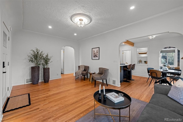 living area featuring arched walkways, light wood-style floors, a textured ceiling, recessed lighting, and baseboards