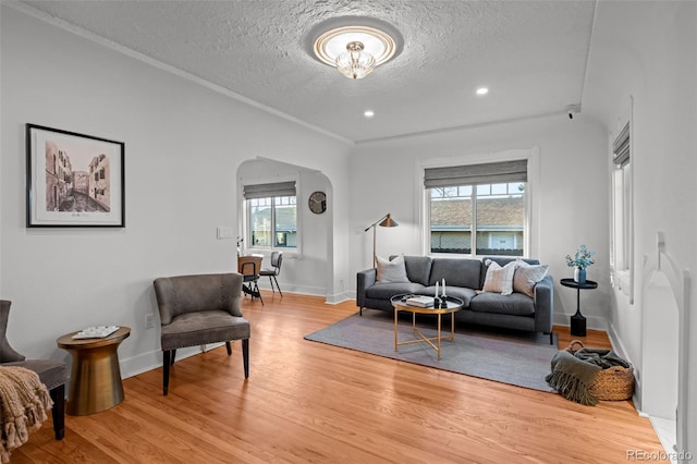 living room featuring arched walkways, a textured ceiling, light wood-type flooring, baseboards, and recessed lighting