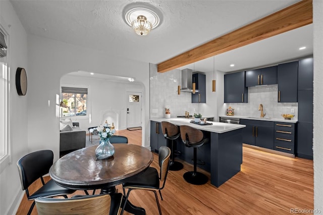 dining area featuring light wood-style flooring, arched walkways, beam ceiling, baseboards, and a textured ceiling