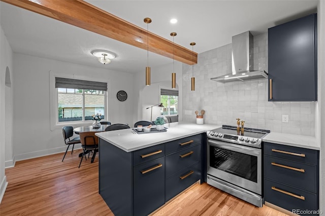 kitchen with stainless steel electric range, wall chimney range hood, blue cabinetry, a peninsula, and decorative backsplash