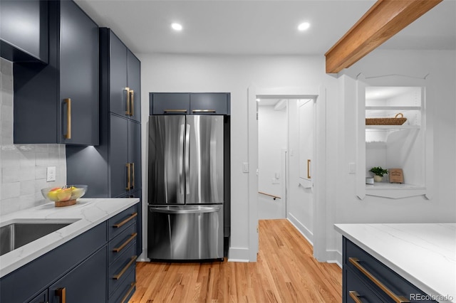 kitchen with freestanding refrigerator, blue cabinets, light wood finished floors, backsplash, and beam ceiling