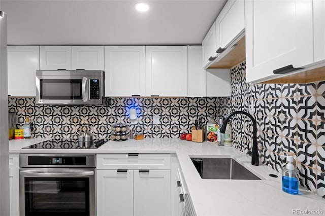 kitchen featuring appliances with stainless steel finishes, a sink, white cabinets, and decorative backsplash