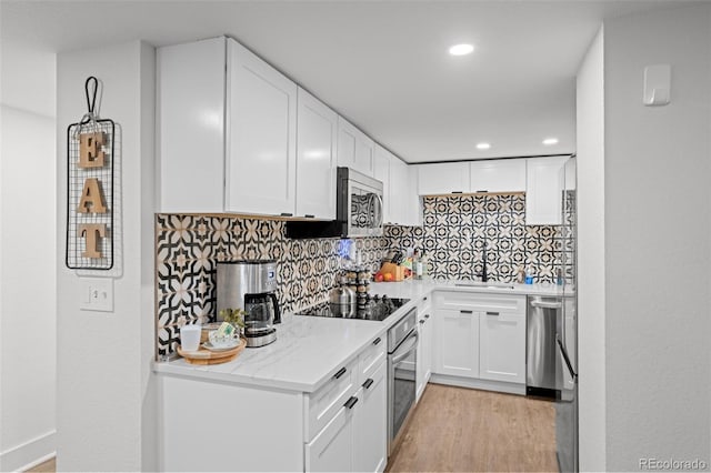 kitchen with stainless steel appliances, a sink, decorative backsplash, white cabinetry, and light wood-style floors