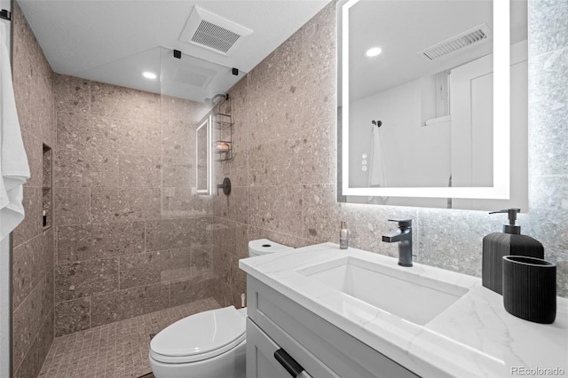 bathroom featuring toilet, tiled shower, vanity, tile walls, and recessed lighting