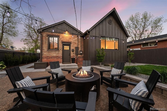 rear view of house with a fire pit, board and batten siding, brick siding, and fence