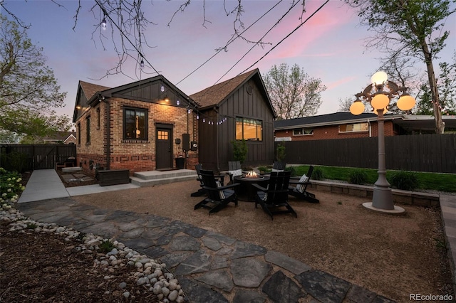 back of property at dusk featuring a fire pit, brick siding, fence, board and batten siding, and a patio area