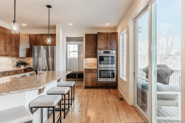 kitchen featuring sink, appliances with stainless steel finishes, hanging light fixtures, light stone counters, and light hardwood / wood-style floors