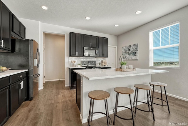 kitchen with stainless steel fridge with ice dispenser, light hardwood / wood-style floors, decorative backsplash, a kitchen island, and range with electric cooktop