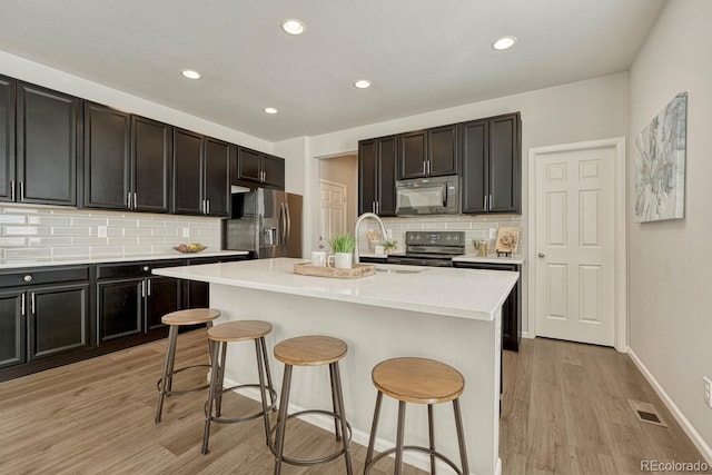 kitchen featuring a center island with sink, backsplash, black appliances, and light wood-type flooring