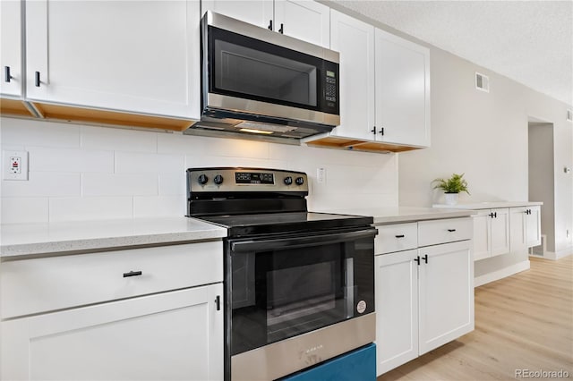 kitchen featuring white cabinetry, tasteful backsplash, a textured ceiling, appliances with stainless steel finishes, and light hardwood / wood-style floors