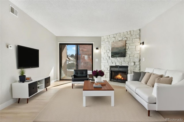 living room featuring a stone fireplace, light hardwood / wood-style floors, and a textured ceiling