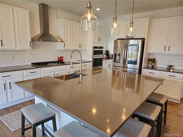 kitchen with appliances with stainless steel finishes, sink, an island with sink, and wall chimney range hood