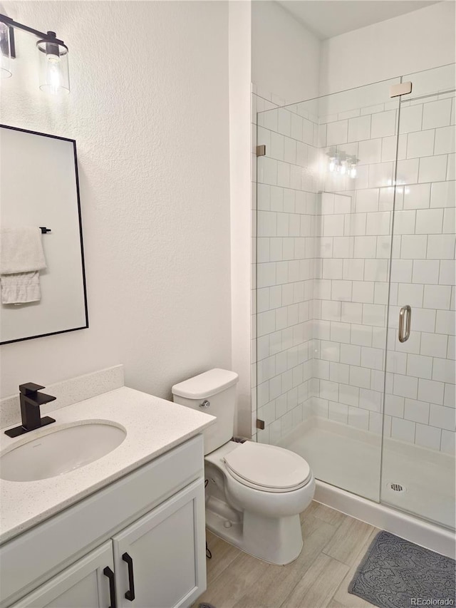 bathroom with hardwood / wood-style floors, vanity, toilet, and a shower with shower door