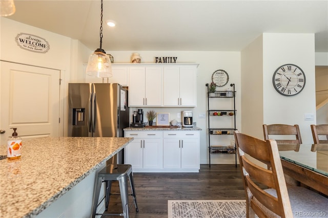 920 William Way, Brighton, CO 80603 - kitchen with stainless steel fridge, dark wood finished floors, white cabinets, a breakfast bar area, and light stone counters