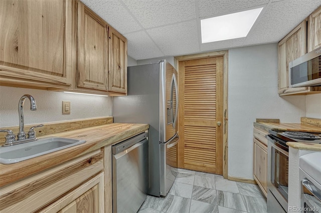 kitchen with a paneled ceiling, stainless steel appliances, butcher block counters, a sink, and baseboards