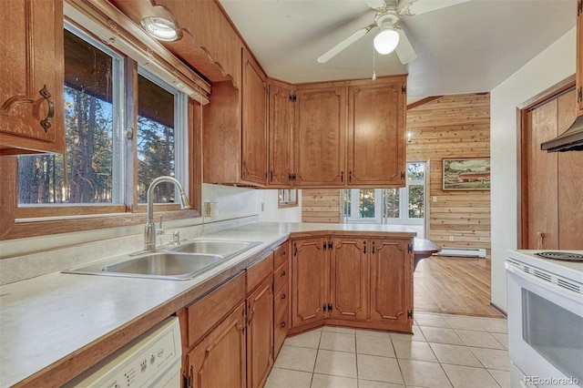 kitchen with light tile patterned floors, light countertops, a sink, wood walls, and white appliances