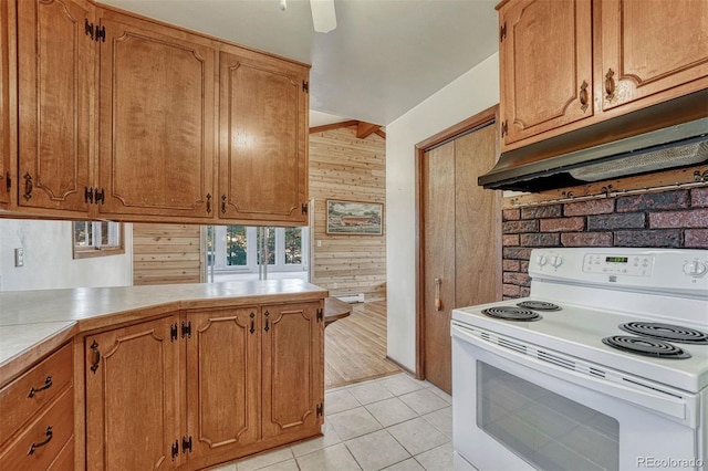 kitchen with light tile patterned floors, wooden walls, under cabinet range hood, electric range, and brown cabinetry