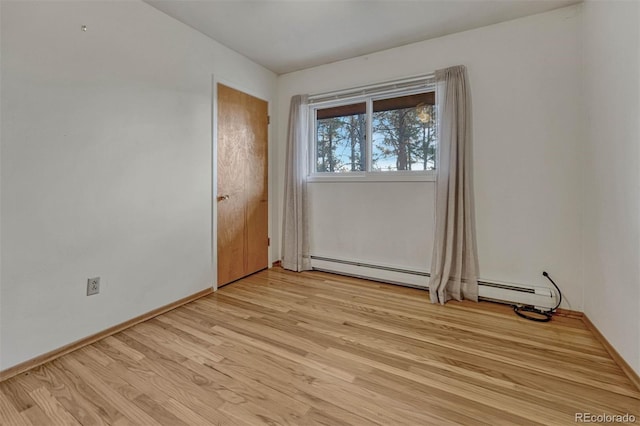 unfurnished room with a baseboard heating unit, baseboards, and light wood-style floors