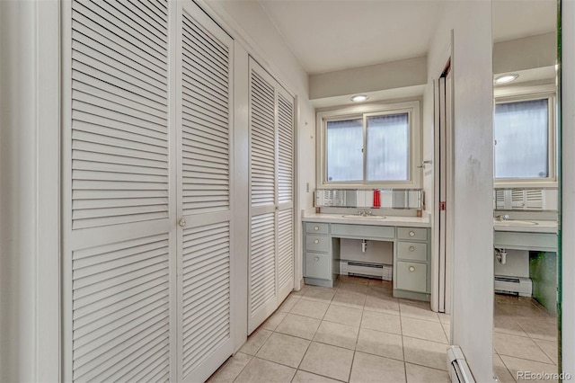 corridor with a baseboard heating unit, a sink, and light tile patterned floors