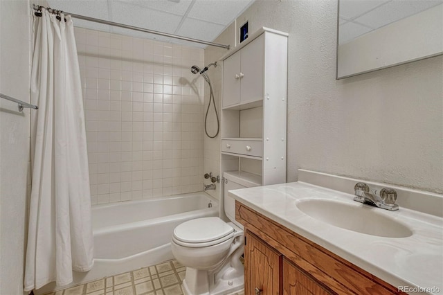 bathroom featuring a textured wall, toilet, shower / bath combo with shower curtain, vanity, and a drop ceiling