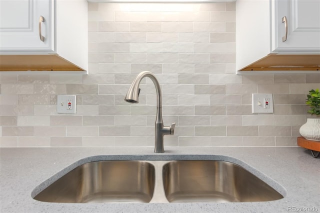 interior details featuring backsplash, white cabinets, and sink