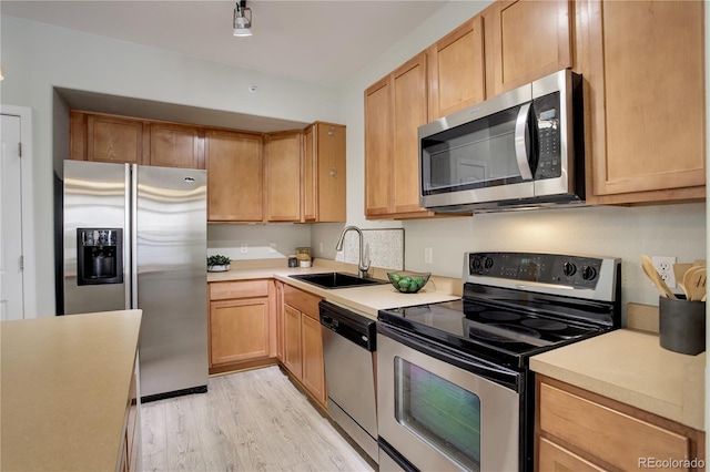 kitchen with light countertops, appliances with stainless steel finishes, light brown cabinets, a sink, and light wood-type flooring