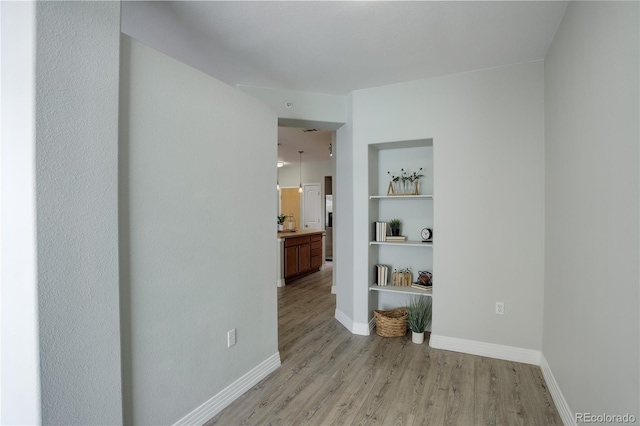 spare room with baseboards, built in features, and light wood-style floors