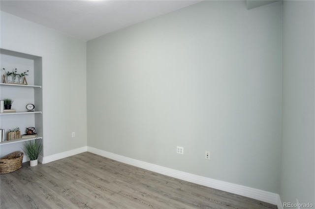 empty room with built in shelves, baseboards, and wood finished floors