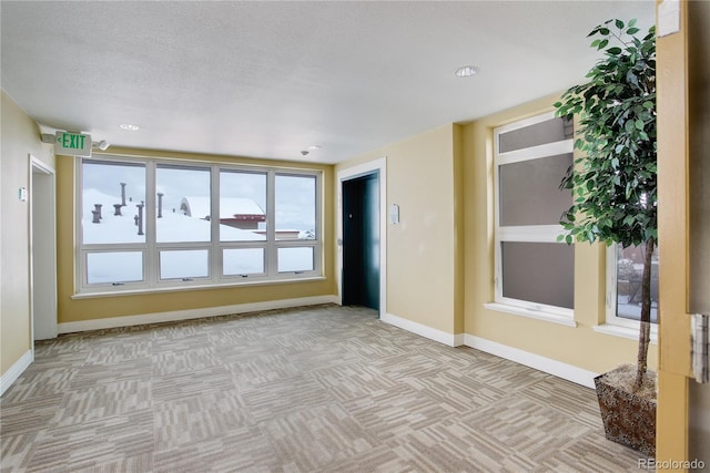 empty room with light colored carpet, a textured ceiling, and baseboards