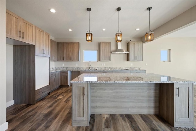 kitchen with dark wood-type flooring, wall chimney exhaust hood, light stone counters, a center island, and pendant lighting