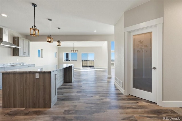 kitchen featuring dark hardwood / wood-style floors, light stone countertops, a center island, and wall chimney exhaust hood