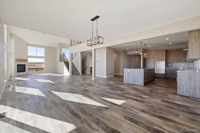 unfurnished living room with dark hardwood / wood-style floors, sink, a stone fireplace, and a notable chandelier