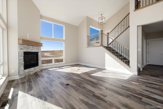 unfurnished living room featuring a stone fireplace, dark wood-type flooring, an inviting chandelier, and a towering ceiling